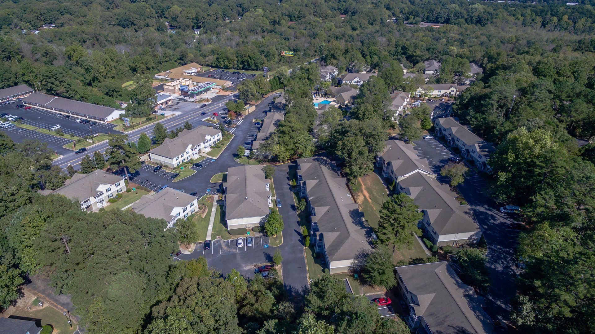Aerial view of a residential apartment complex surrounded by dense green trees and interconnected parking lots.