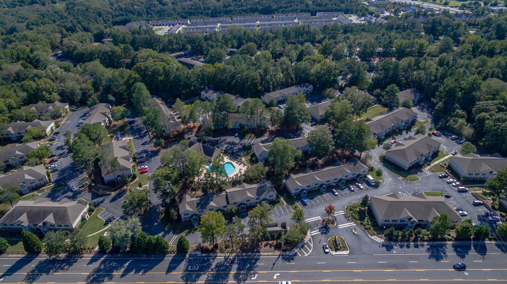 Aerial view of a residential apartment complex with multiple buildings, a swimming pool, and parking lots near a road.