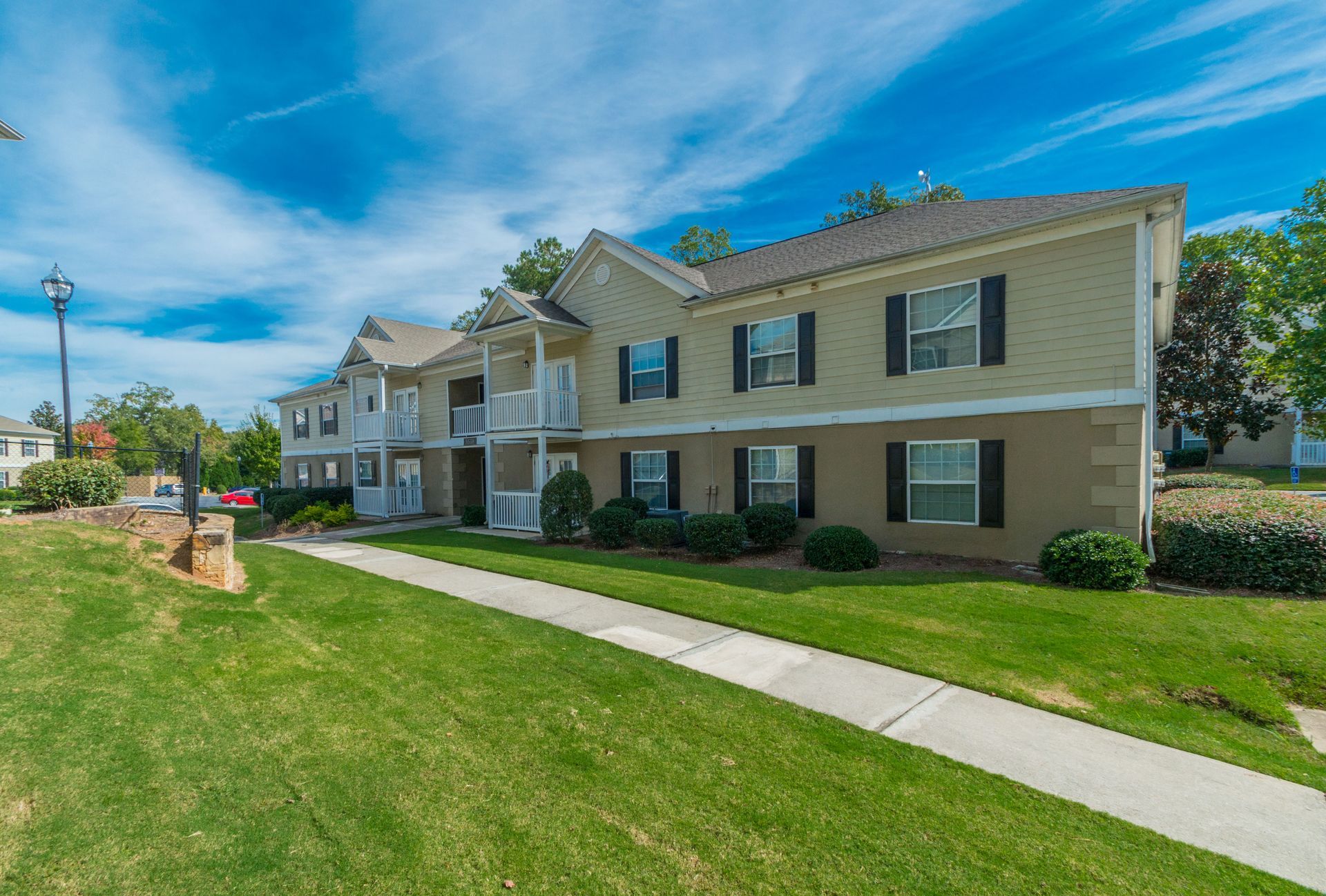 A two-story apartment complex with light yellow siding and a concrete walkway on a sunny day with a blue sky.