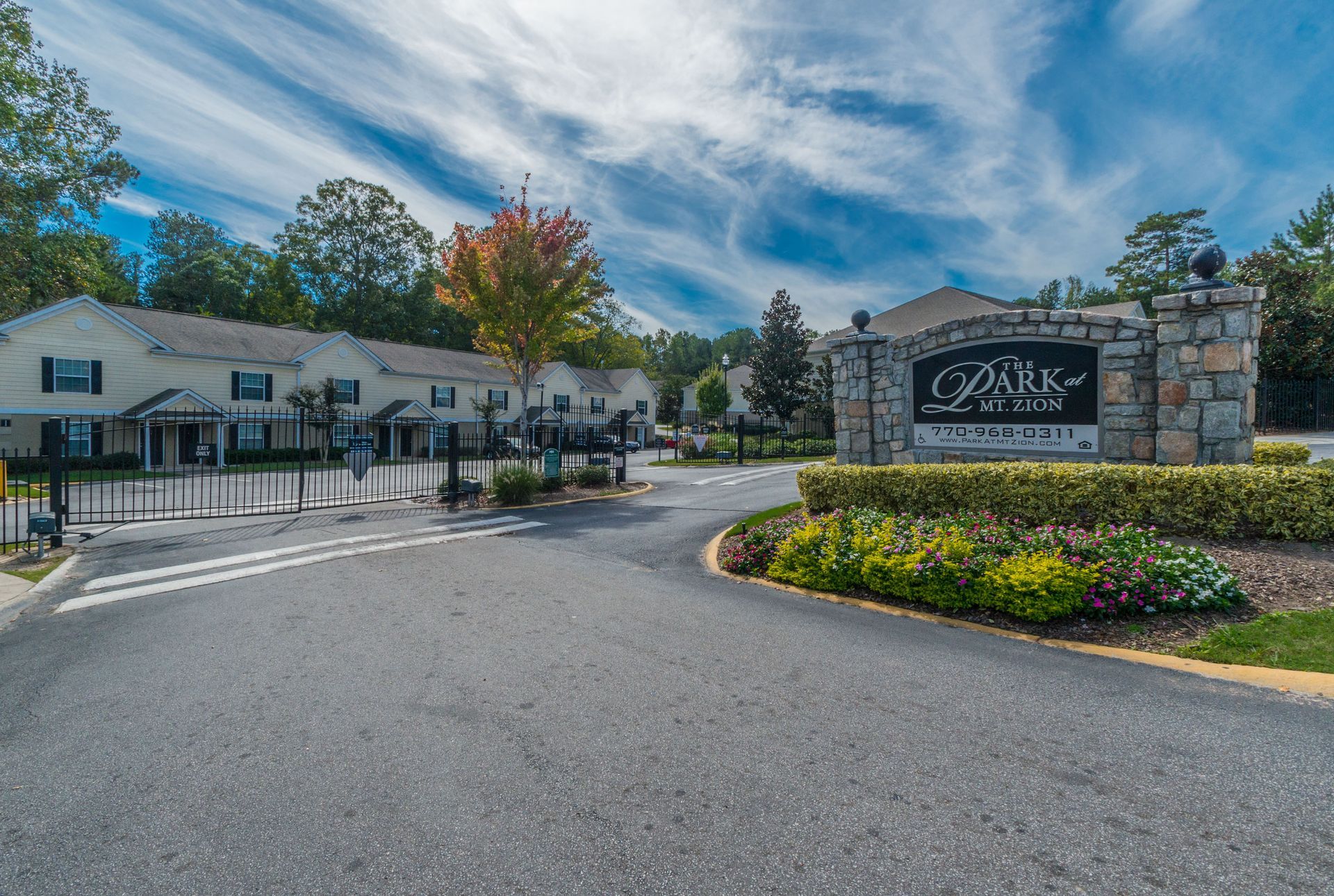 The gated entrance to The Walk at Braeburn apartments, featuring a stone sign and beige residential buildings.