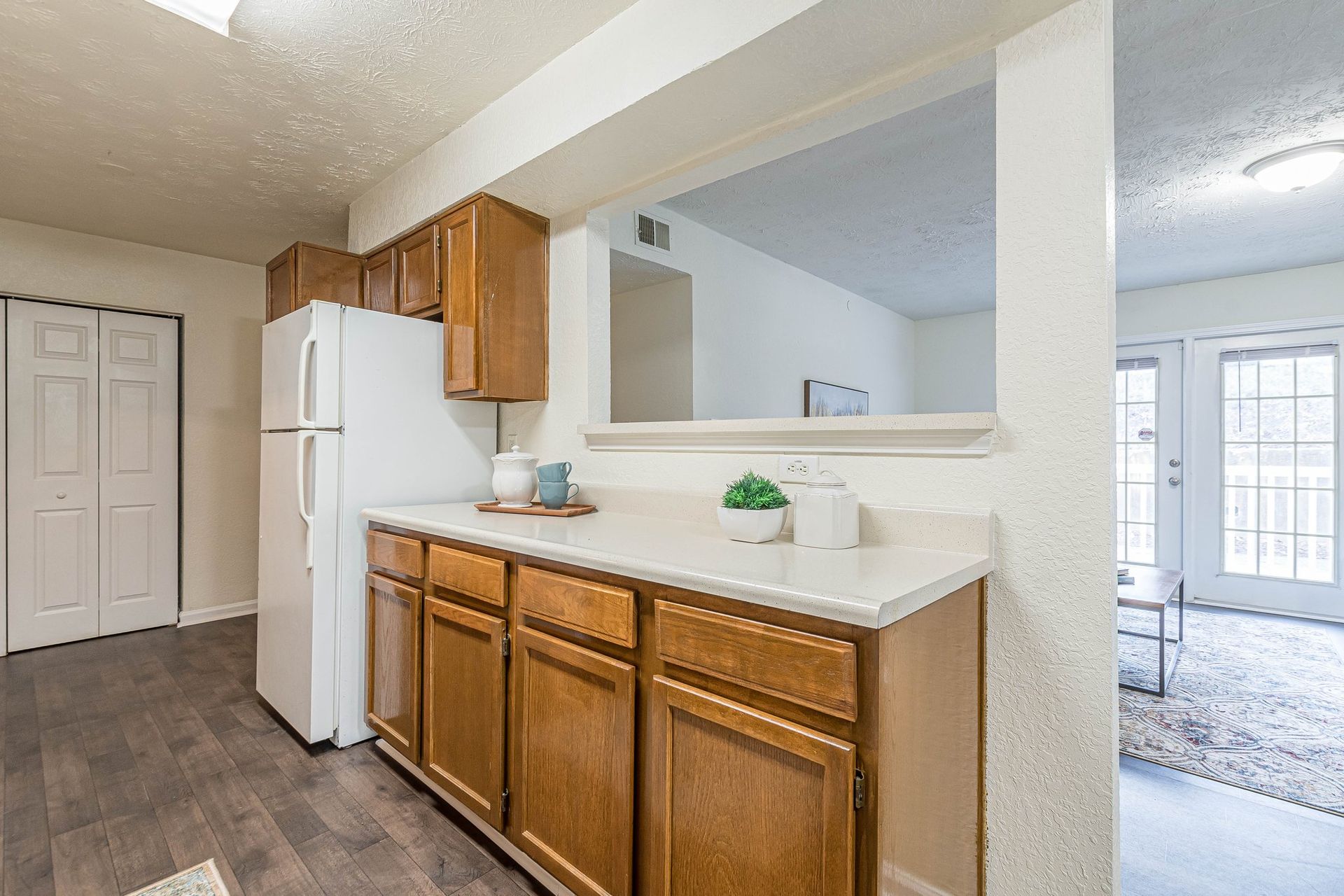 A kitchen with oak cabinets, a white refrigerator, and a countertop with decor, opening into a living room with glass doors.
