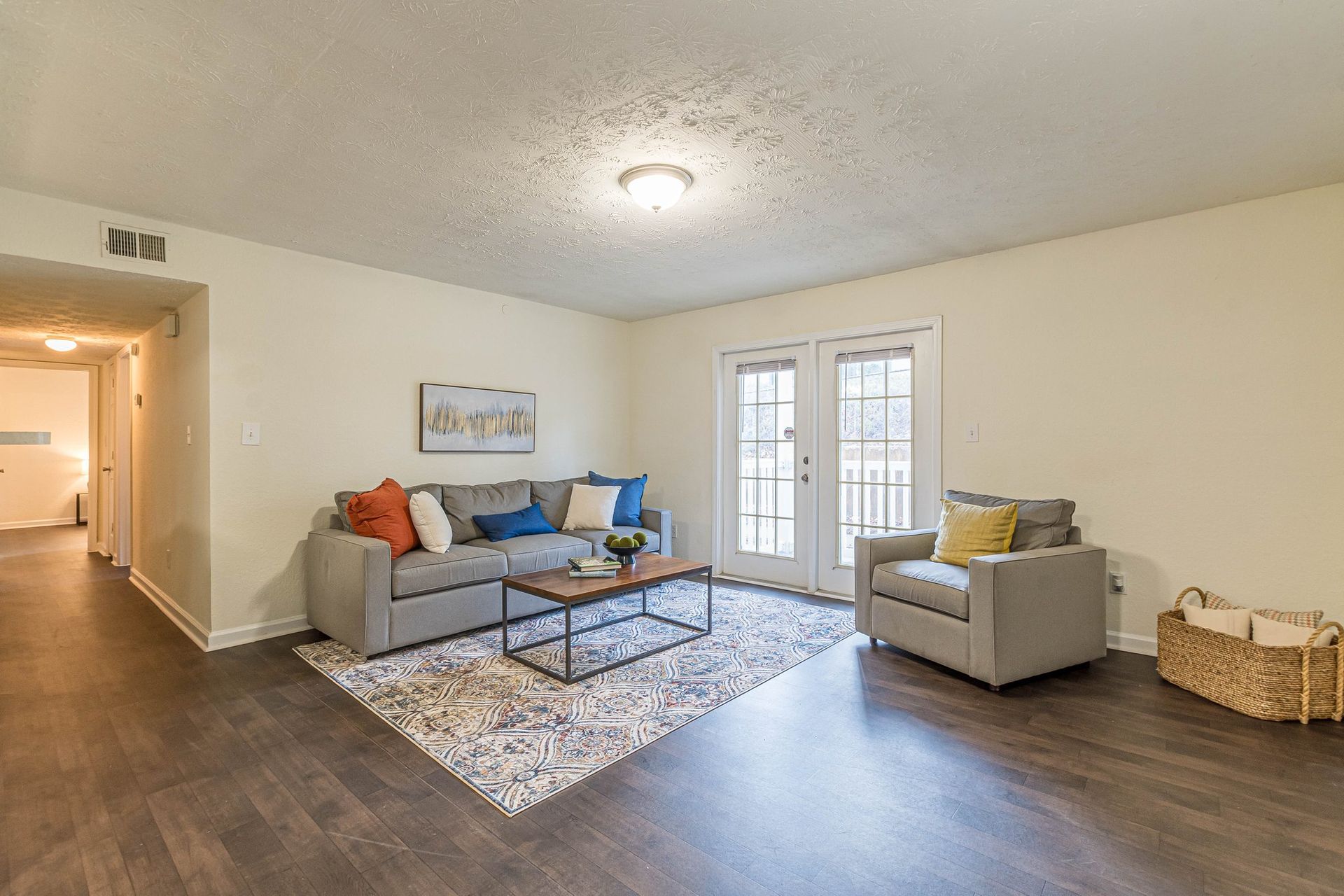 A living room with a gray sofa, patterned rug, wood coffee table, gray armchair, and sliding glass doors.