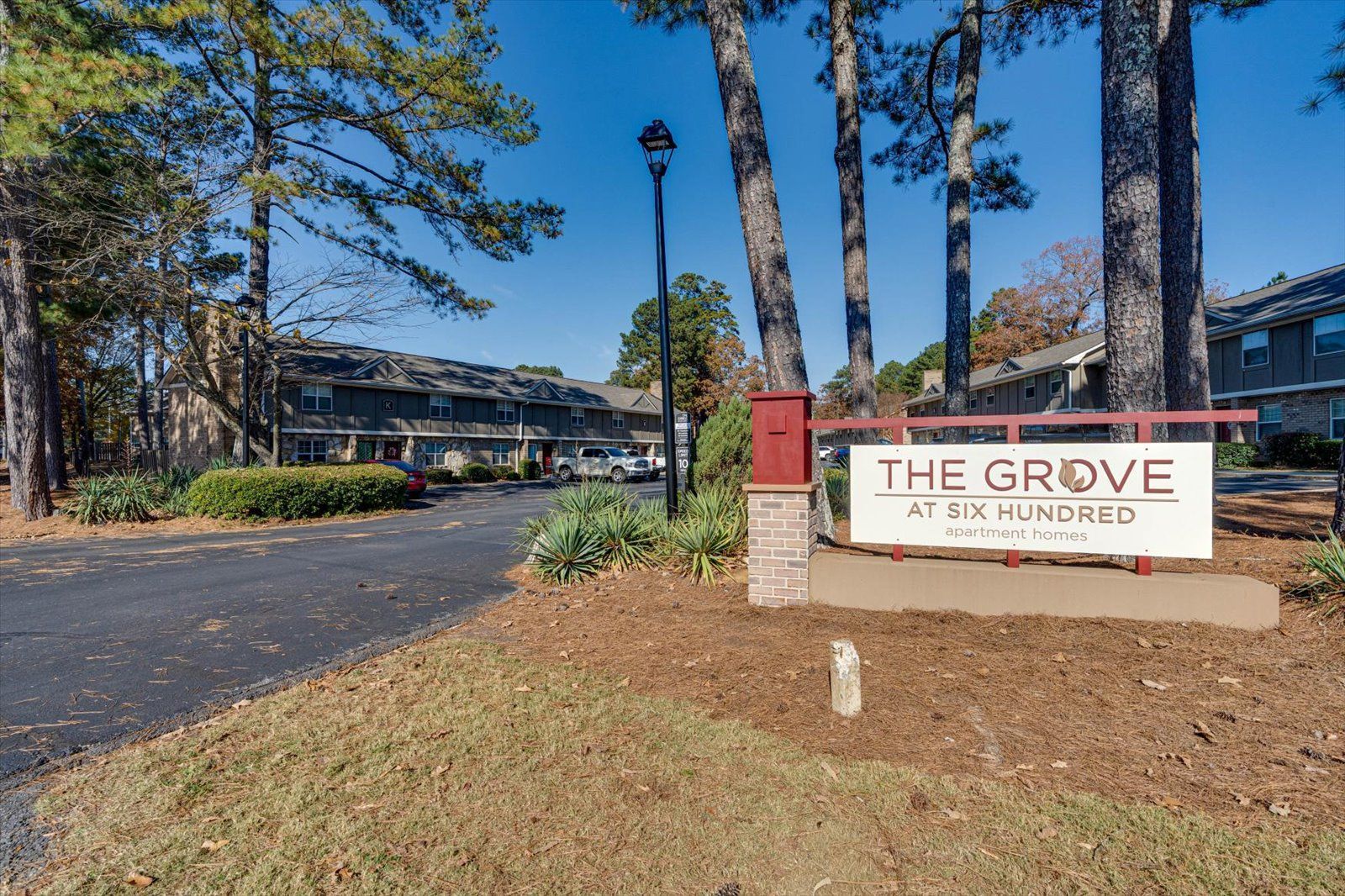 The Grove at White Oaks entrance sign beside trees and a driveway on a sunny day