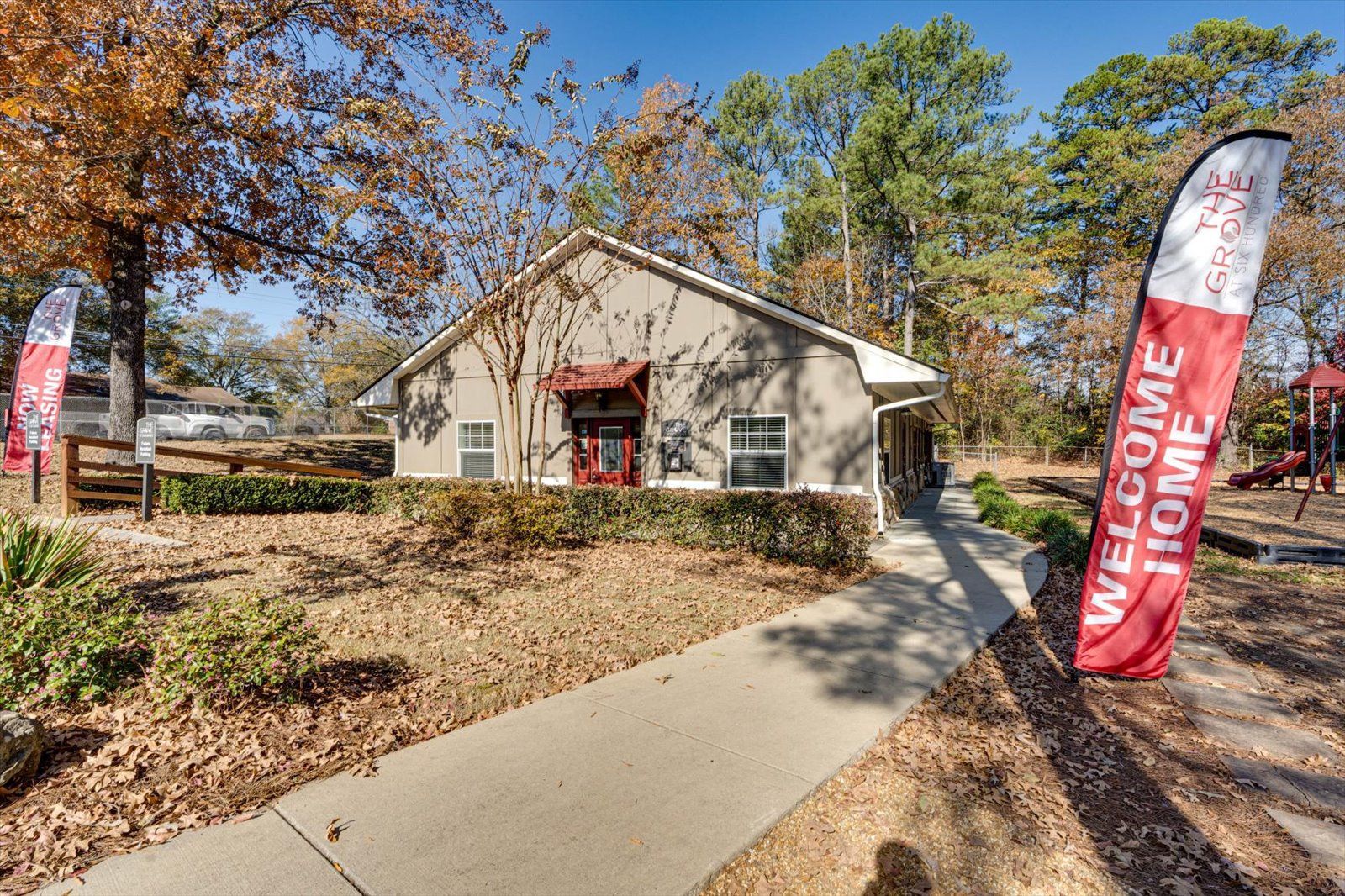 Small building with a red door and welcome flags along a sidewalk in a wooded area