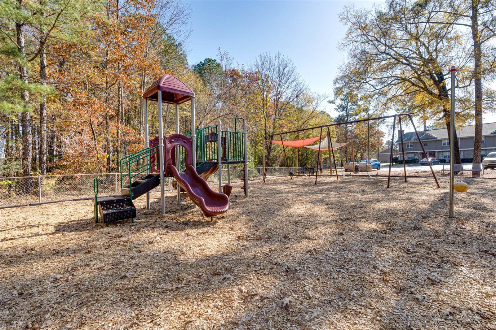 Empty playground with red slide and climbing structure in a leaf-covered park in autumn