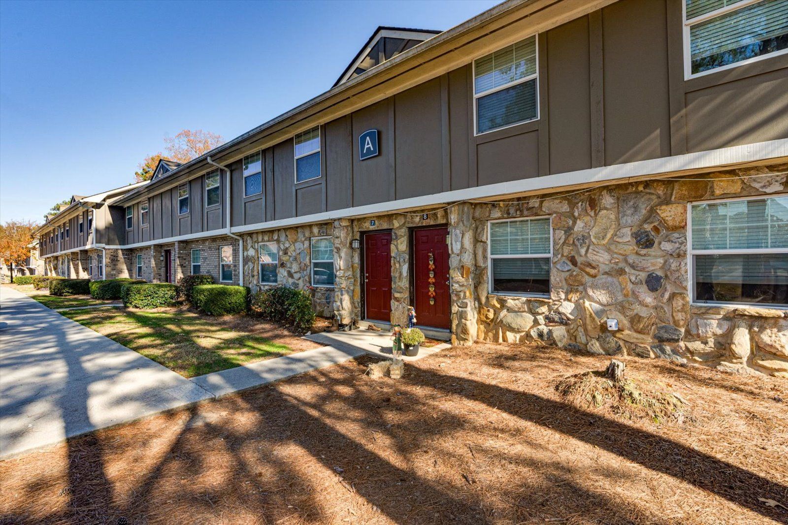 Exterior of a two-story apartment building with stone and tan siding, red doors, and a sidewalk along the front