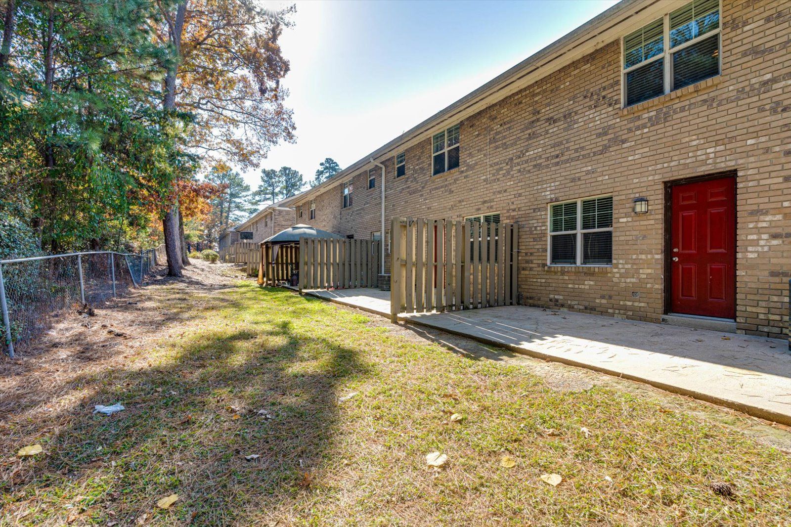 Brick apartment building with red door, windows, and grassy courtyard in sunlight