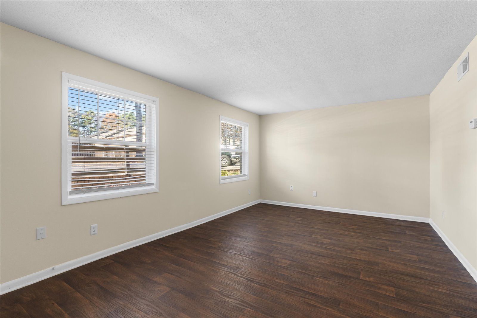 Empty beige room with dark wood floors and two windows letting in daylight