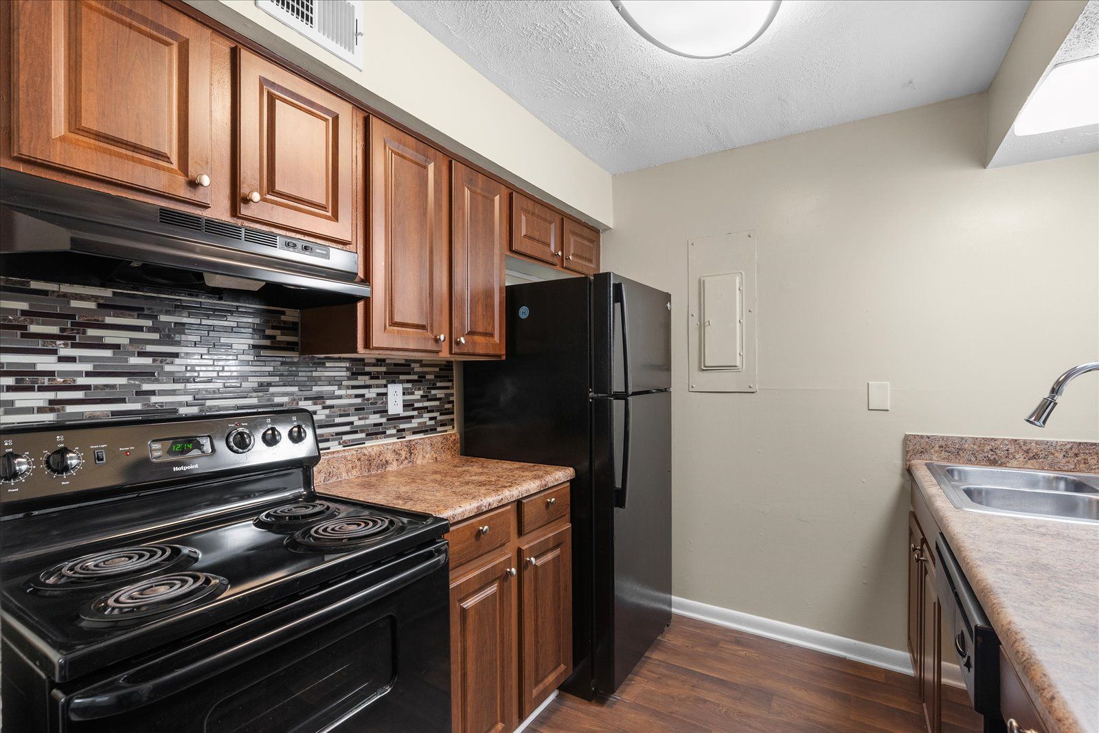 Kitchen with black stove and refrigerator, wood cabinets, tile backsplash, and a countertop sink.