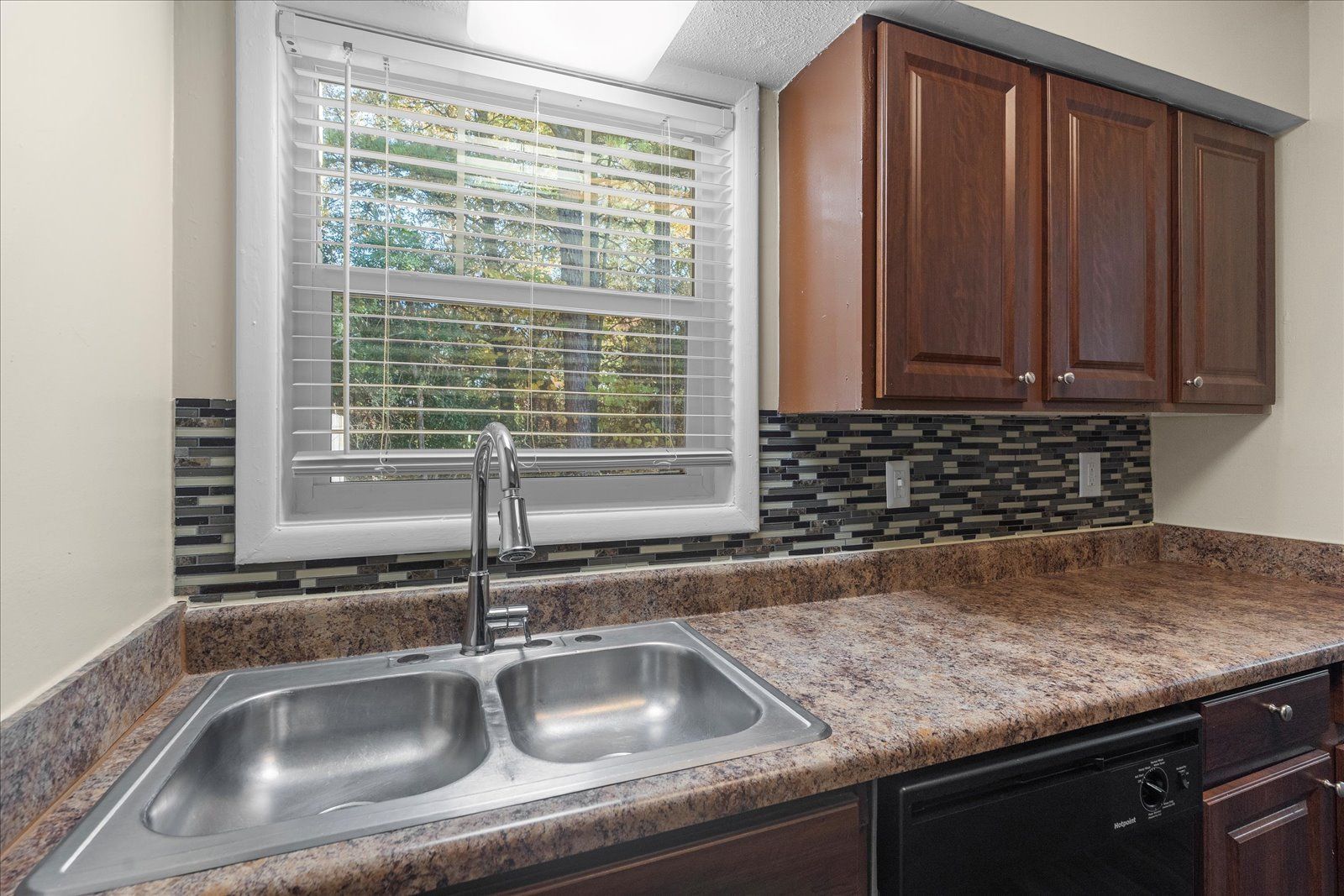 Kitchen sink under window with blinds, granite countertop, and dark wood cabinets