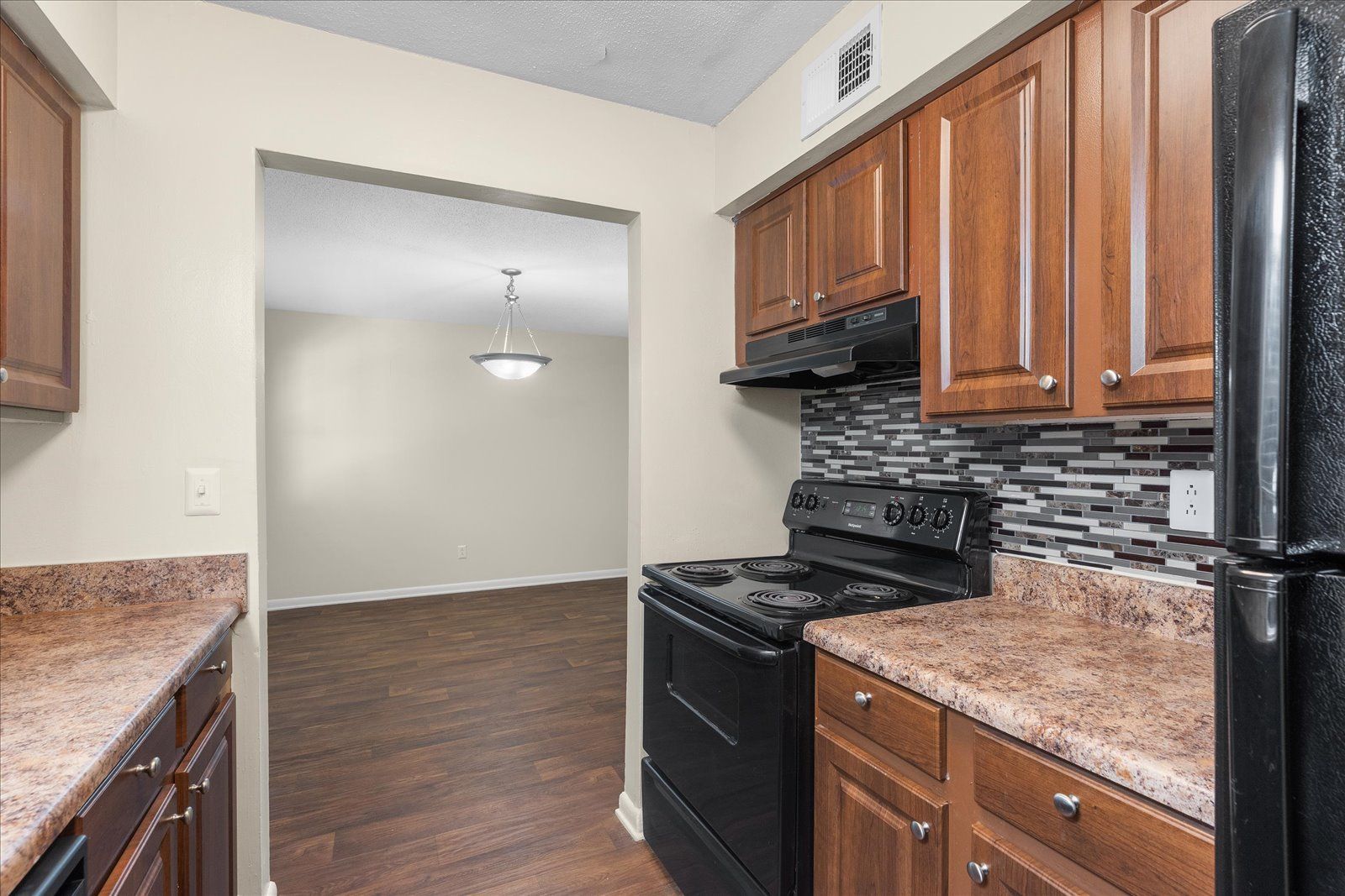 Kitchen with dark wood cabinets, black stove, and brown granite counters opening to a dining area