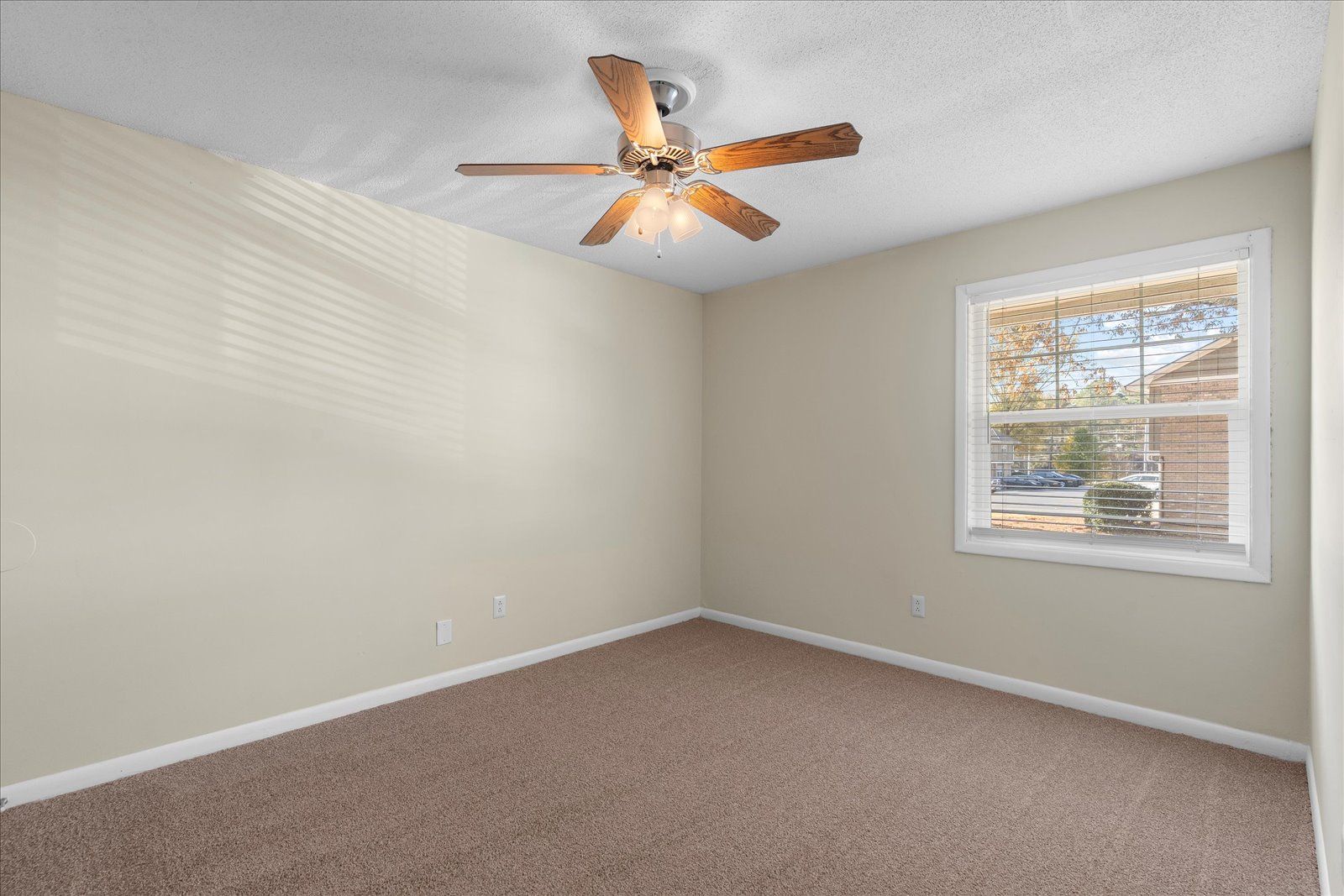 Empty beige bedroom with carpet, ceiling fan, and a window letting in daylight
