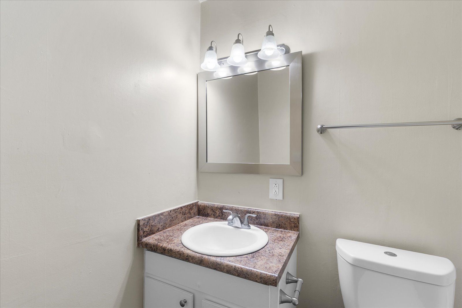 Small bathroom vanity with white sink, mirror, three-light fixture, and toilet