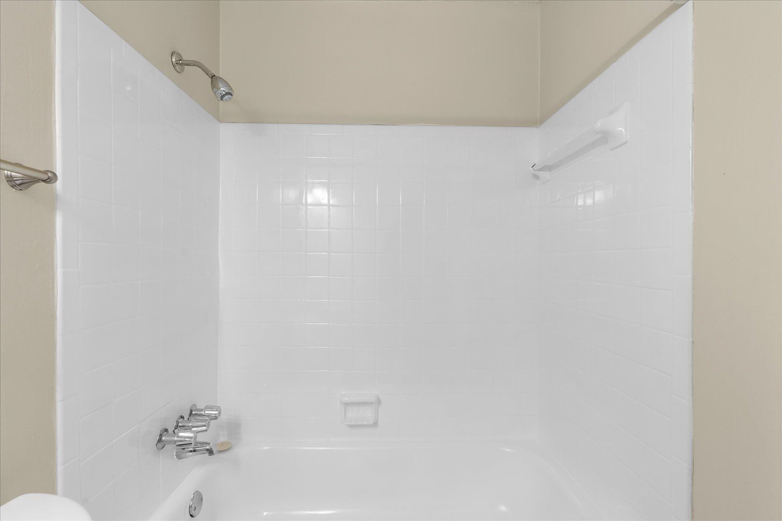 Empty white bathtub/shower with tiled walls and chrome fixtures