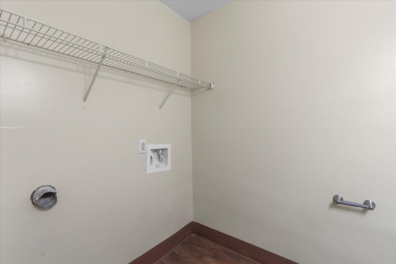 Empty laundry room with wire shelf, utility hookups, and beige walls.