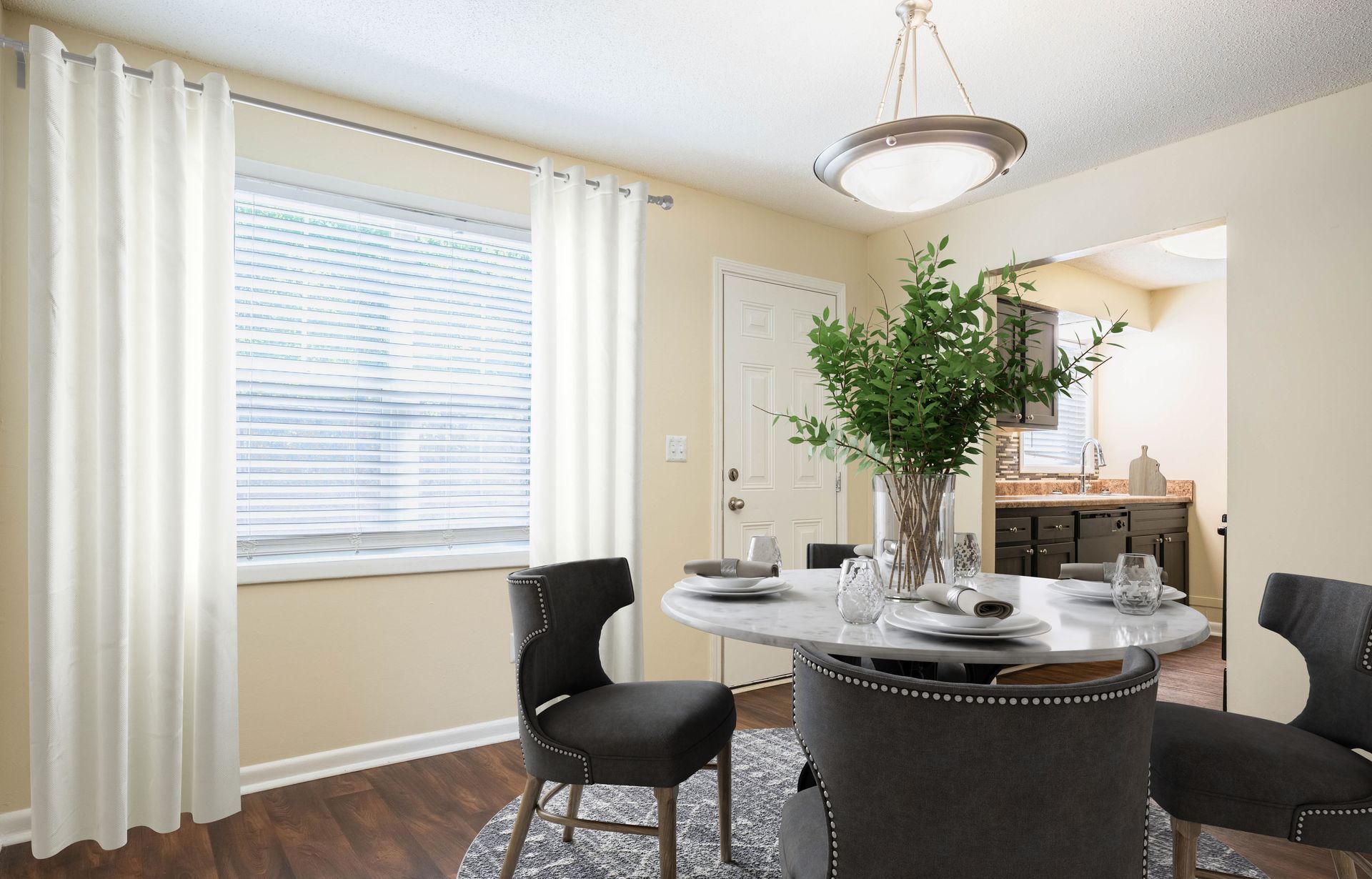 Bright dining room with round table, dark chairs, white curtains, and a large potted plant