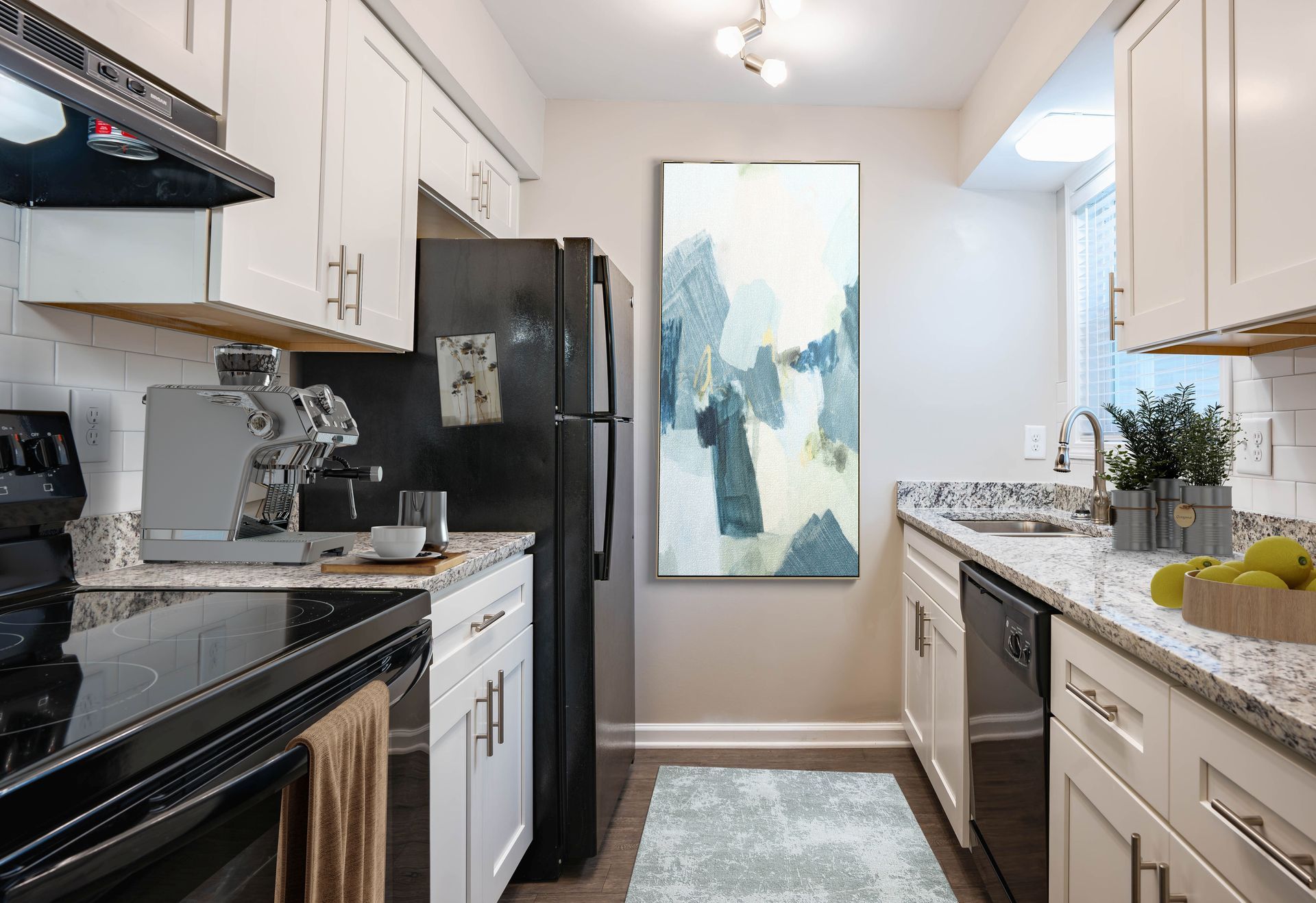 Bright galley kitchen with white cabinets, black appliances, granite counters, and abstract wall art.