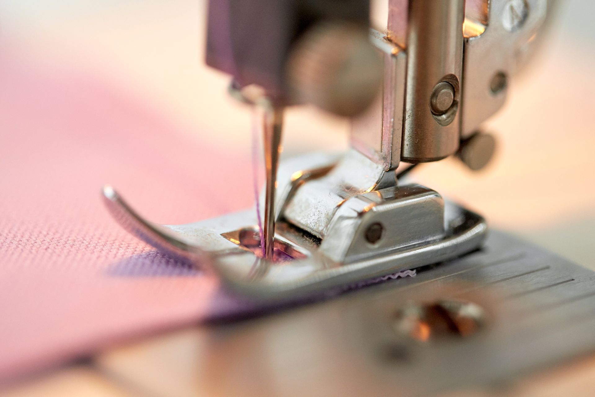 Close-up of a sewing machine needle and presser foot with blue thread spools nearby