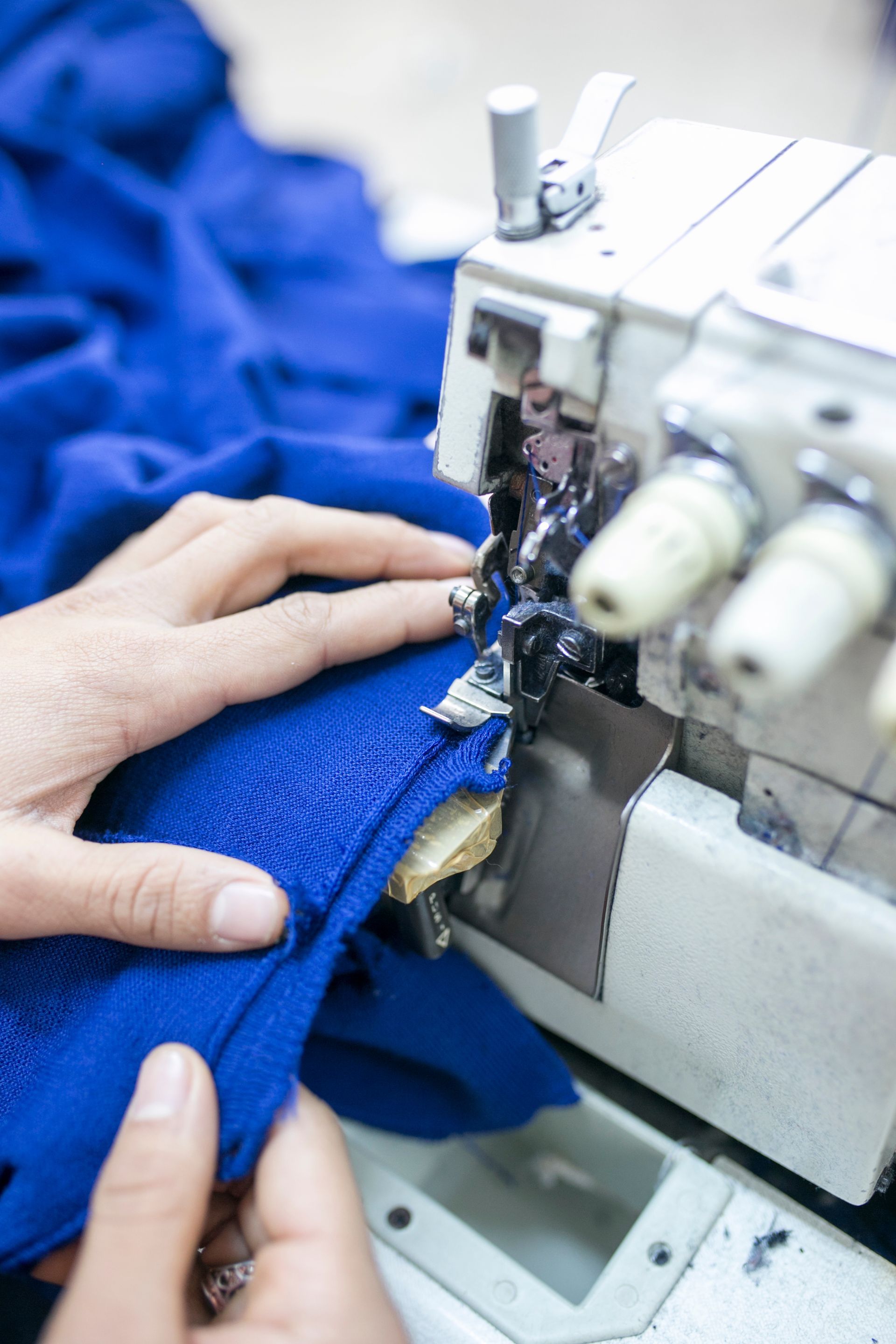 Hands guiding blue fabric through a sewing machine as it stitches the material.