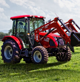 Red tractor with front loader parked on a grassy field under a cloudy sky