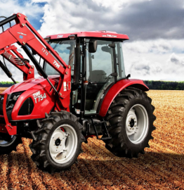 Red tractor with front loader working in a muddy field under cloudy sky