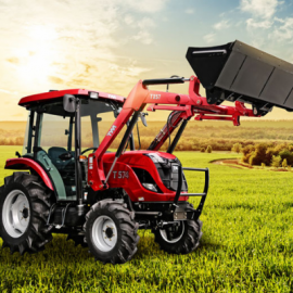 Red tractor with front loader lifting a black bucket in a green field at sunset