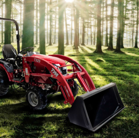 Red tractor with front loader in a sunlit forest clearing