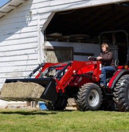 Man on red tractor moving hay bale out of a white barn doorway