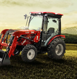 Red tractor with front loader driving through a field at sunset