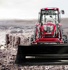 Red tractor with front loader driving through muddy field under overcast sky