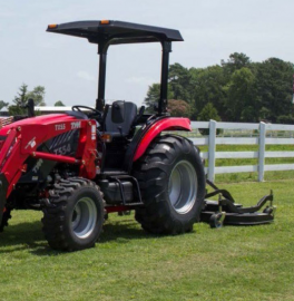 Red tractor with mower attachment on a grassy field beside a white fence