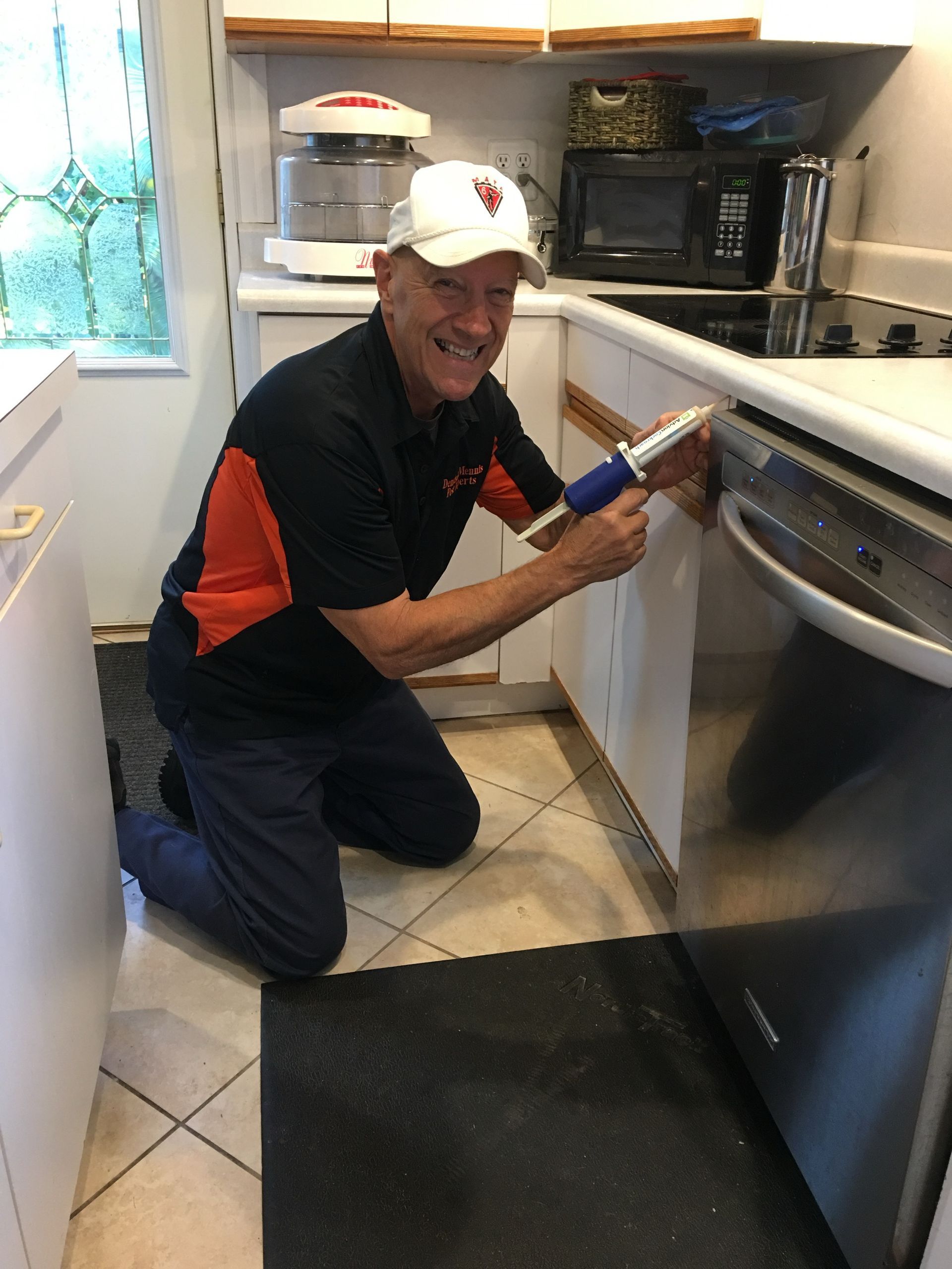 Person kneeling and using a tool to fix an appliance in a kitchen