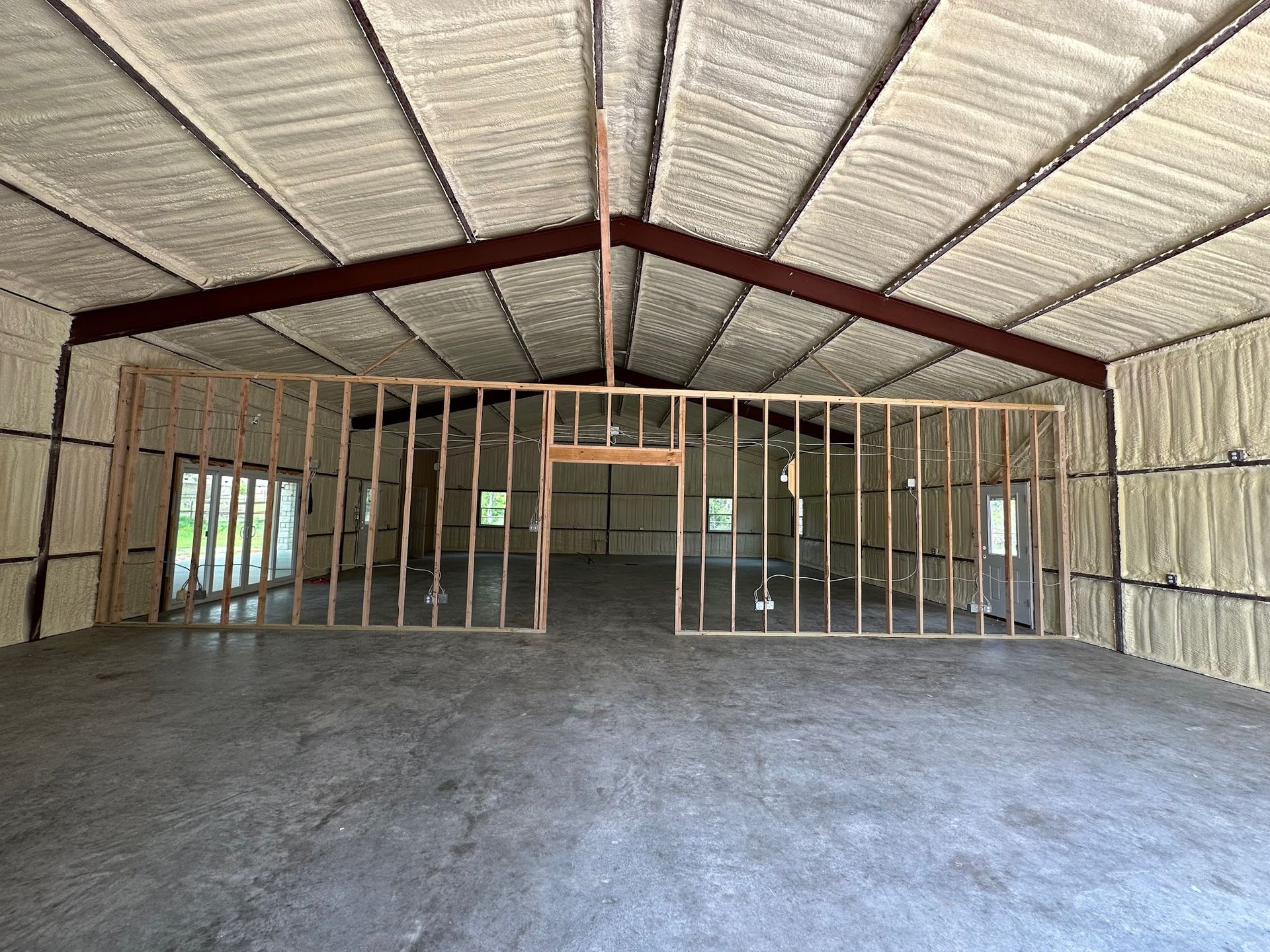 Interior of a metal building with spray foam insulation and framed walls on a concrete floor.