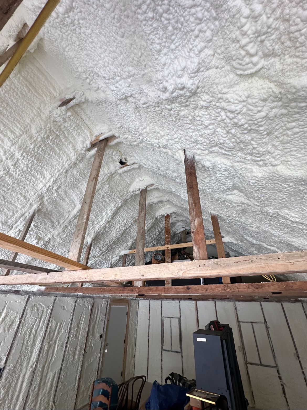 Attic with spray foam insulation on roof and walls, wooden beams visible.