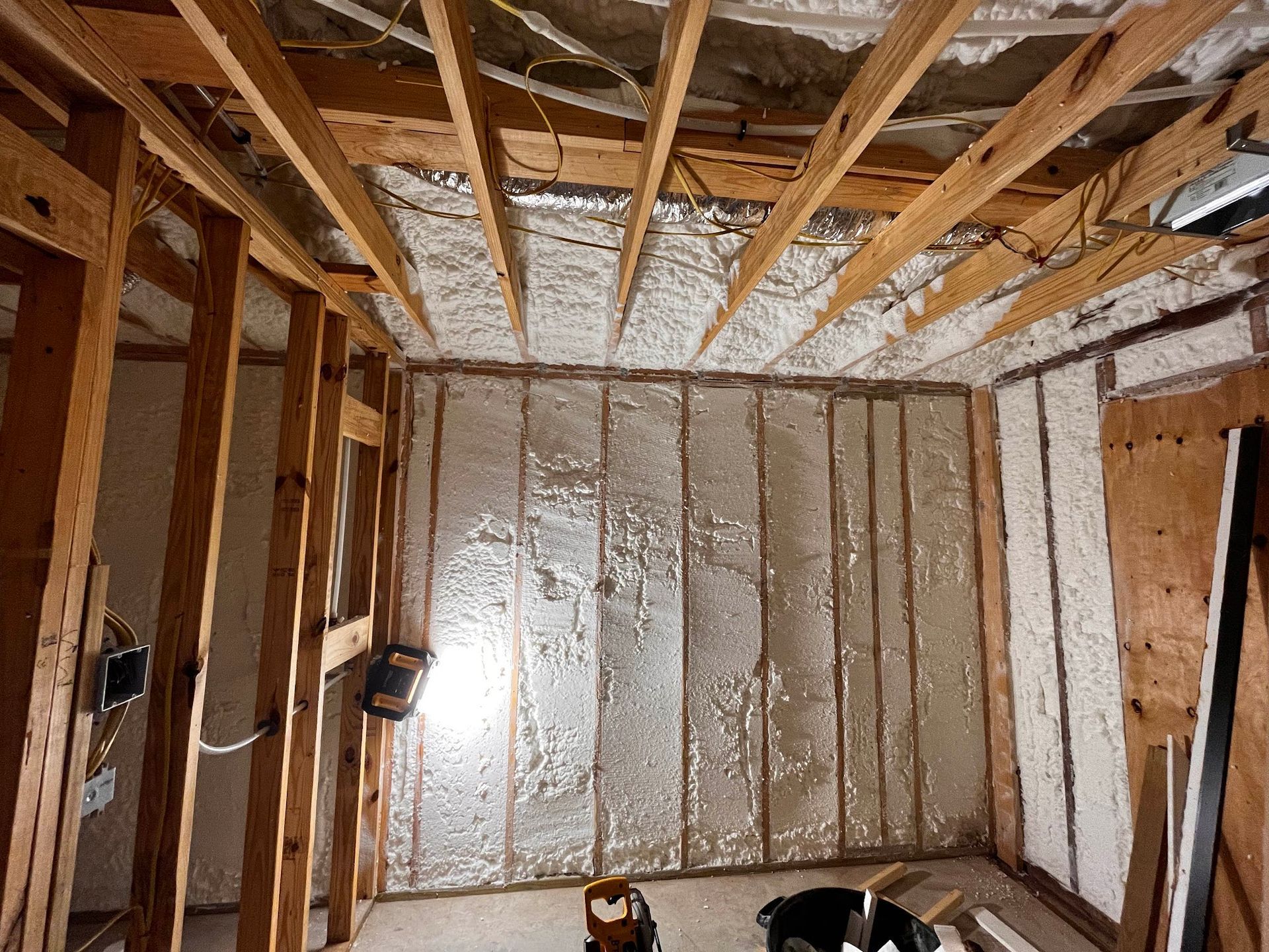 Interior view of a room under construction, walls and ceiling covered in insulation. Wooden beams are visible.