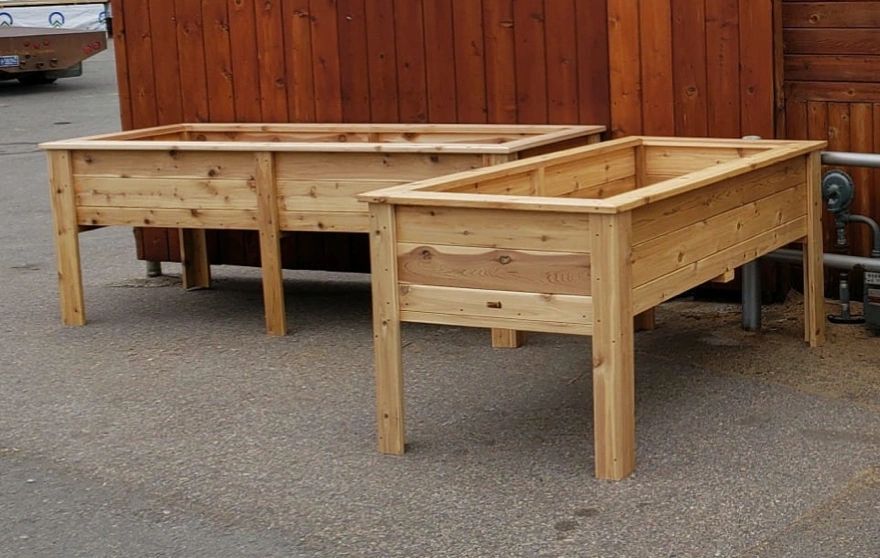 Two wooden planters are sitting on the ground in front of a wooden fence.