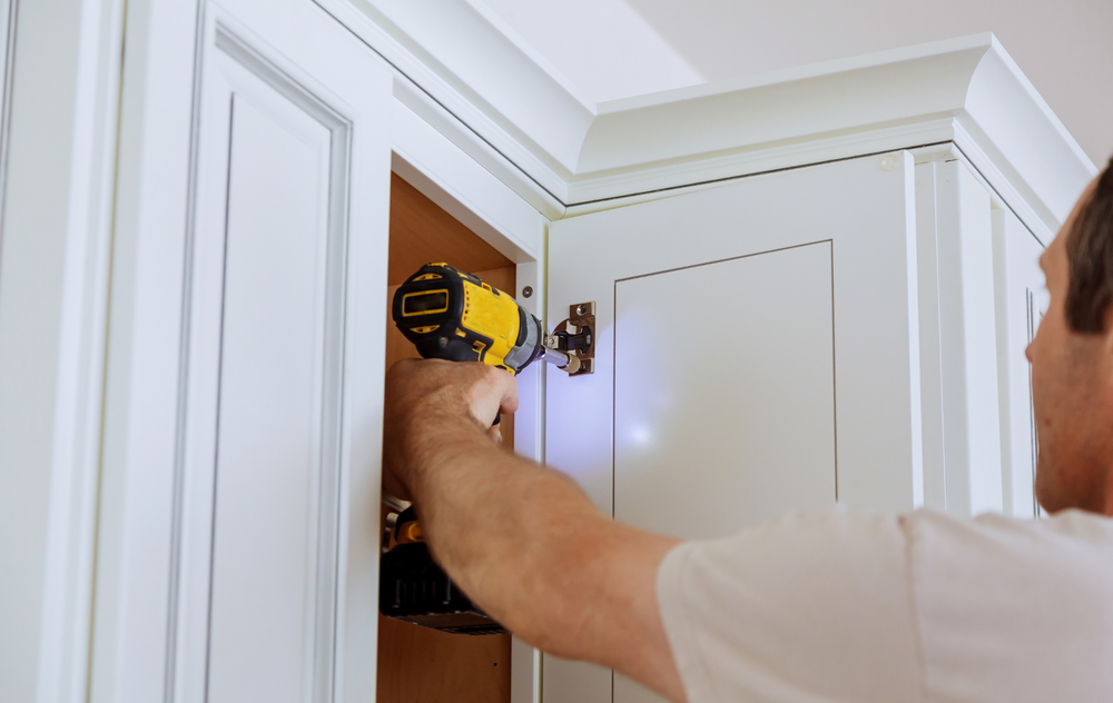 A man is using a drill to install cabinet doors in a kitchen.