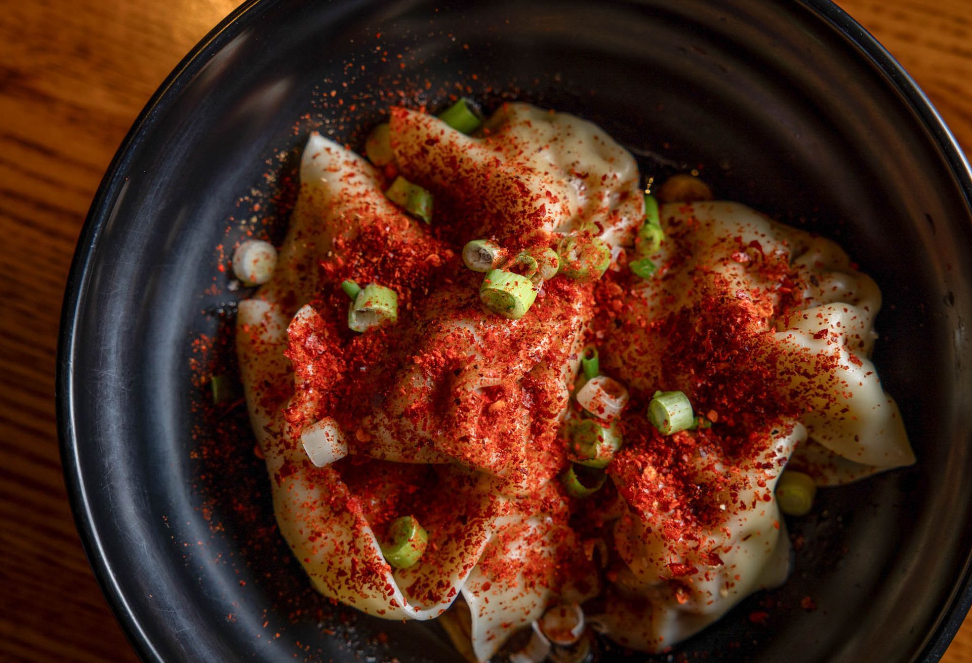 Bowl of dumplings topped with red spice and chopped green onions