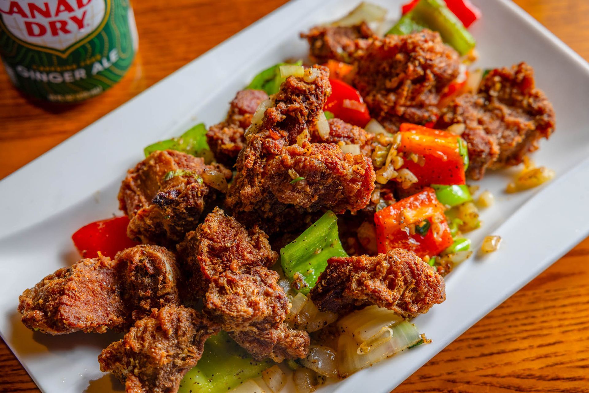 Fried chicken pieces on a white platter with red and green bell peppers, garnished with herbs.