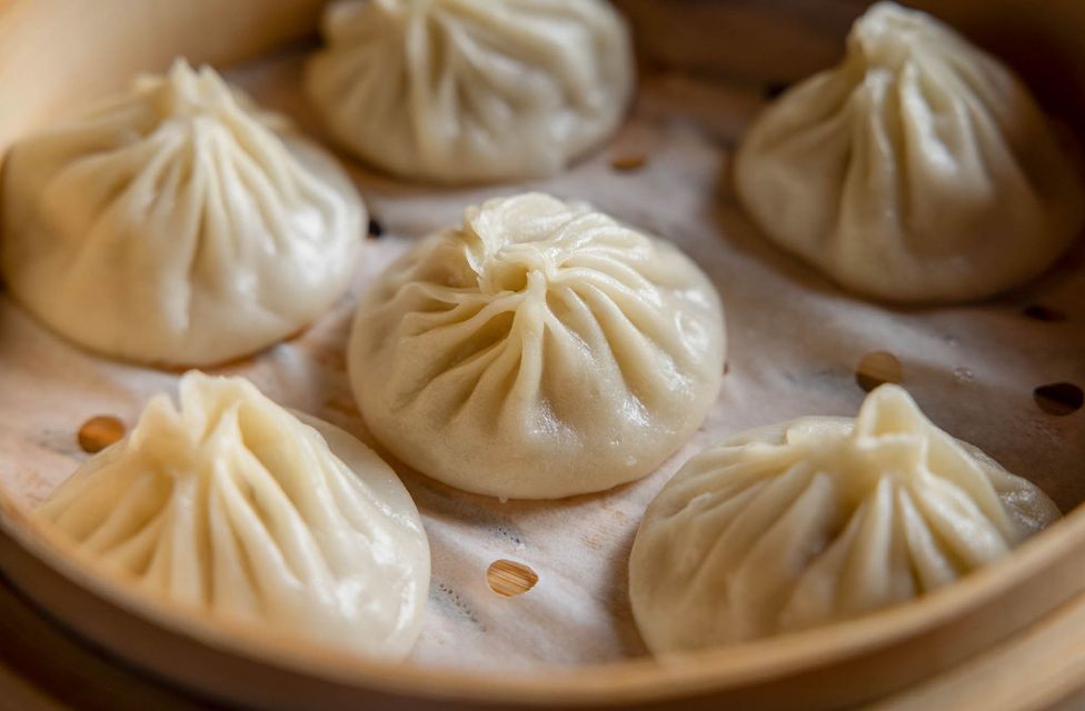 Steamed dumplings in a bamboo basket, topped with pleated folds and arranged in a circle