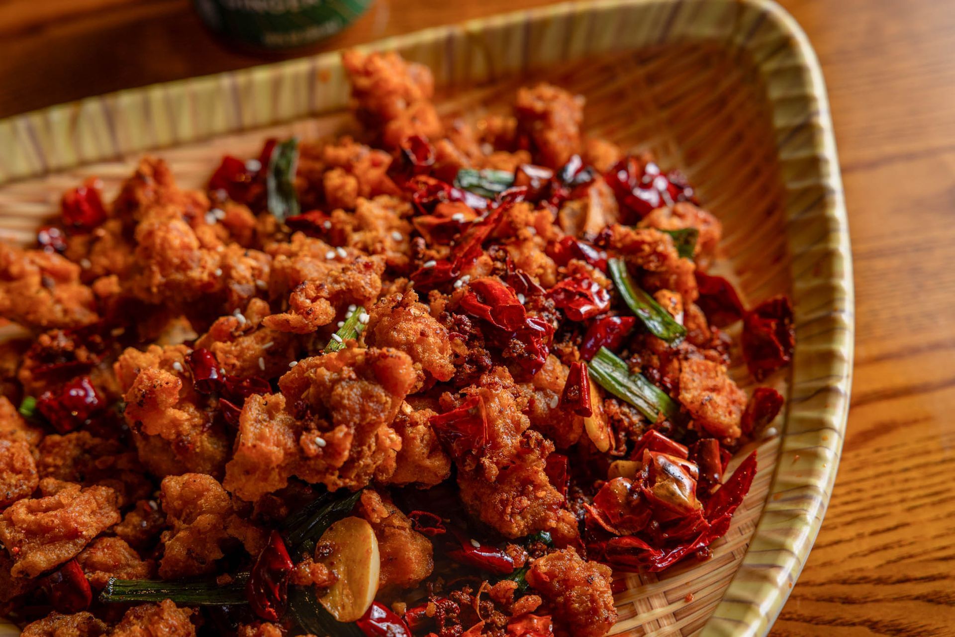 Tray of crispy fried chicken tossed with red chilies and green herbs on a woven plate