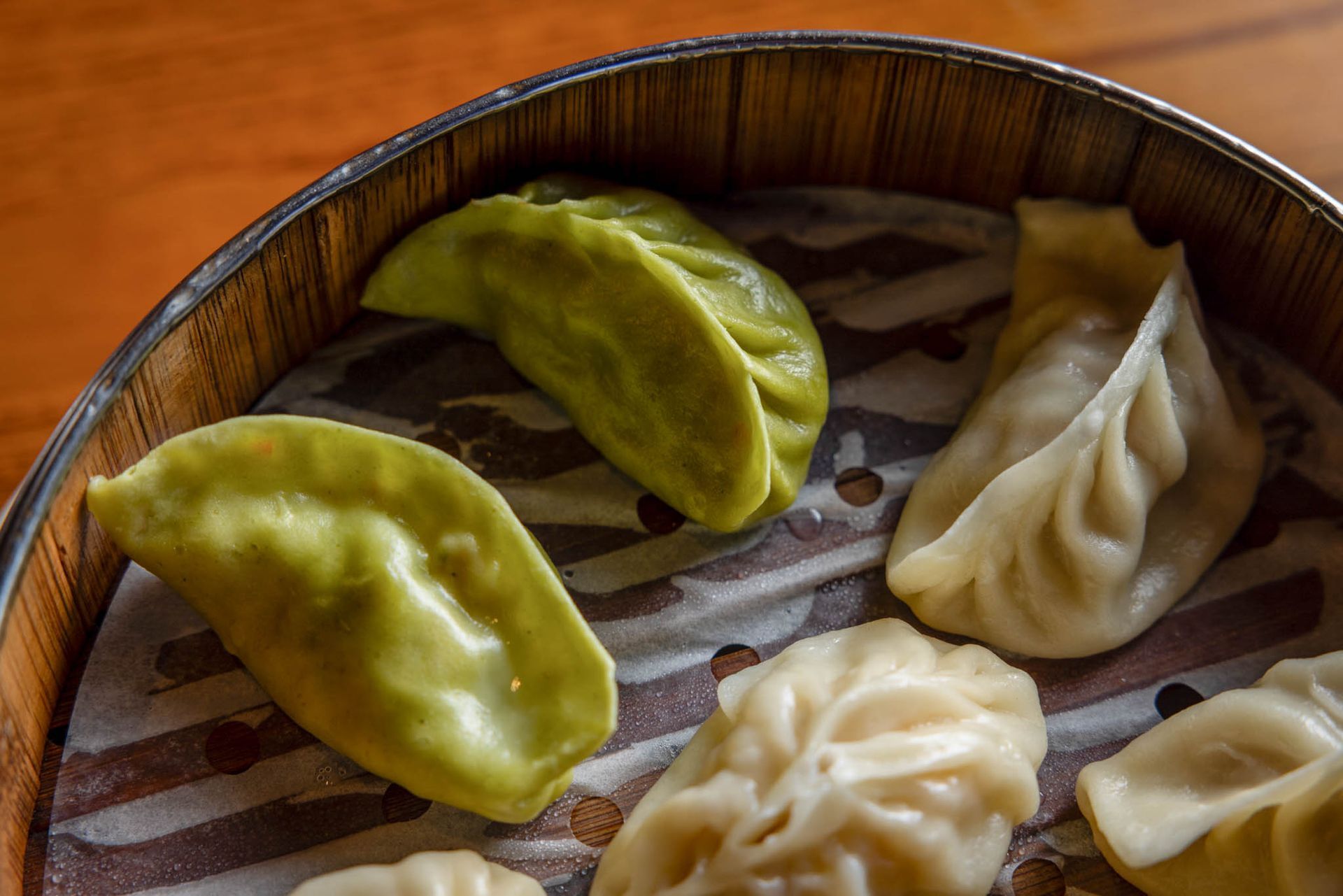 Wooden tray of assorted dumplings, including green and beige crescent-shaped pieces.