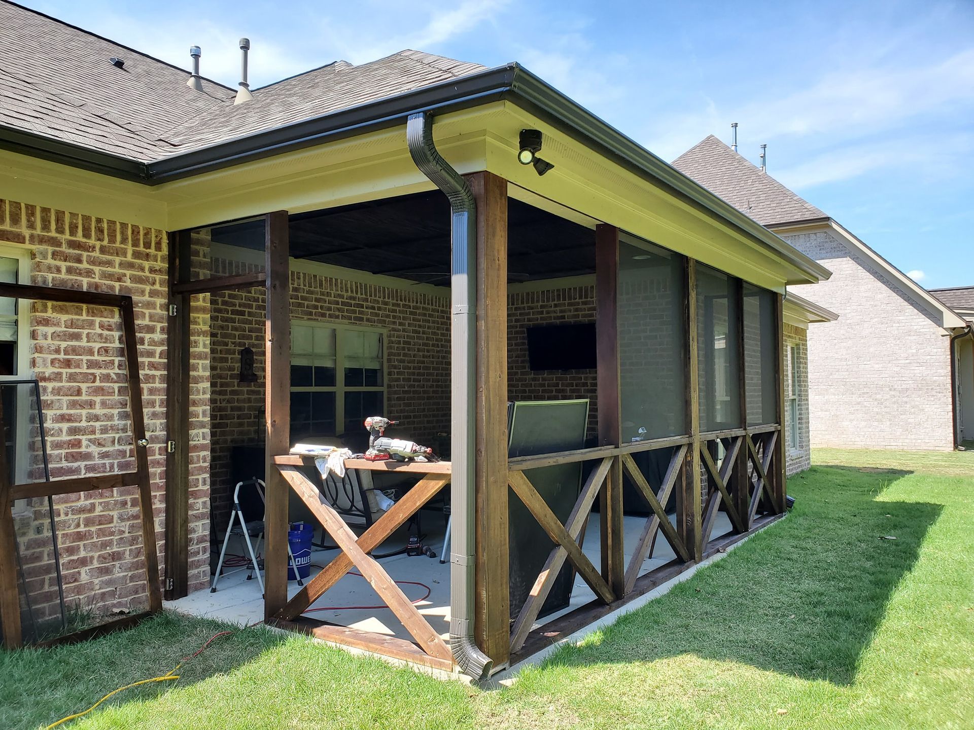 A screened in porch is being built in the backyard of a brick house.