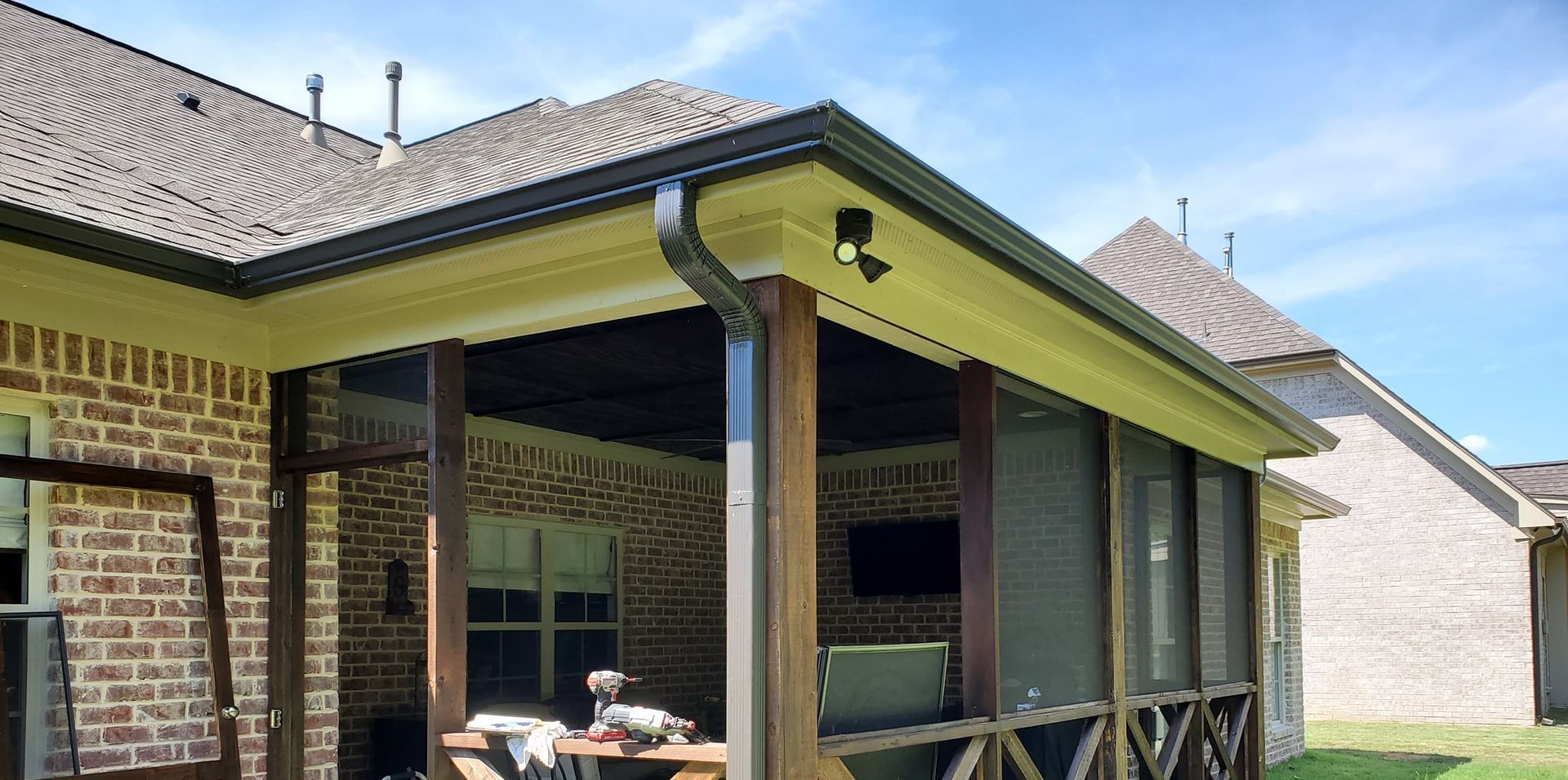 A screened in porch with a brick house in the background.