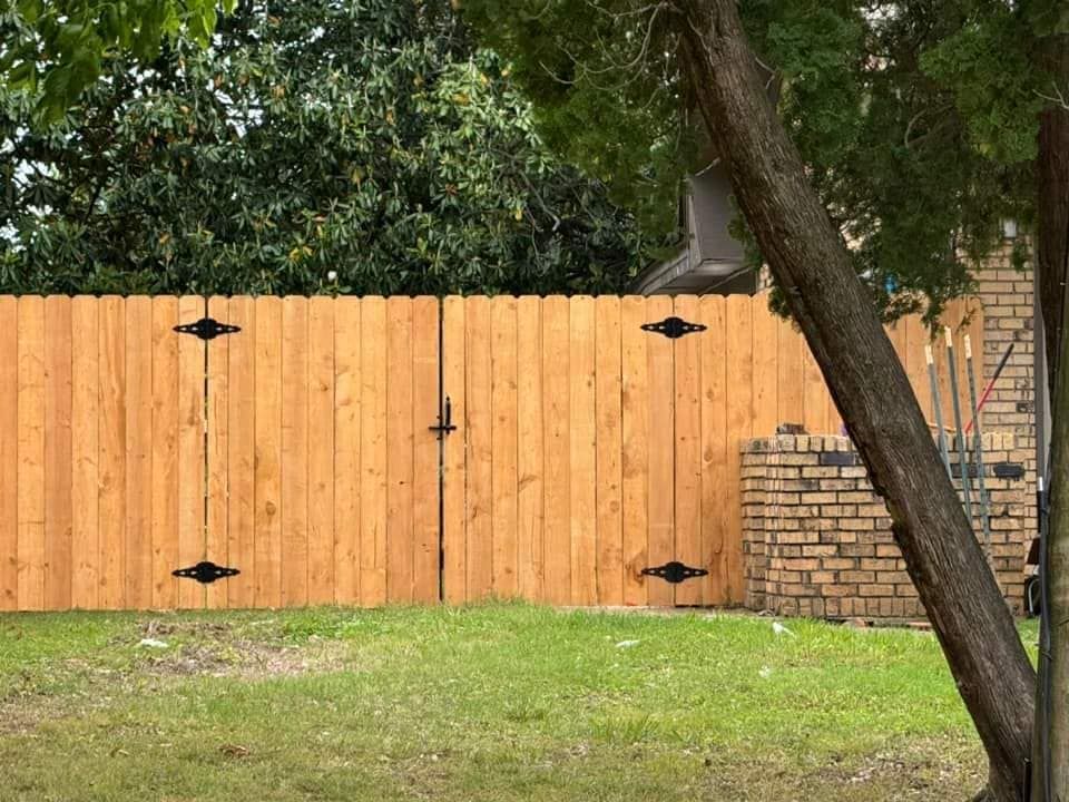 A wooden fence is surrounded by grass and trees in a backyard.
