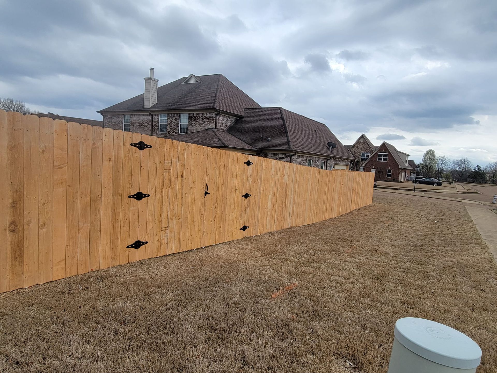 A wooden fence surrounds a large house in a residential area.