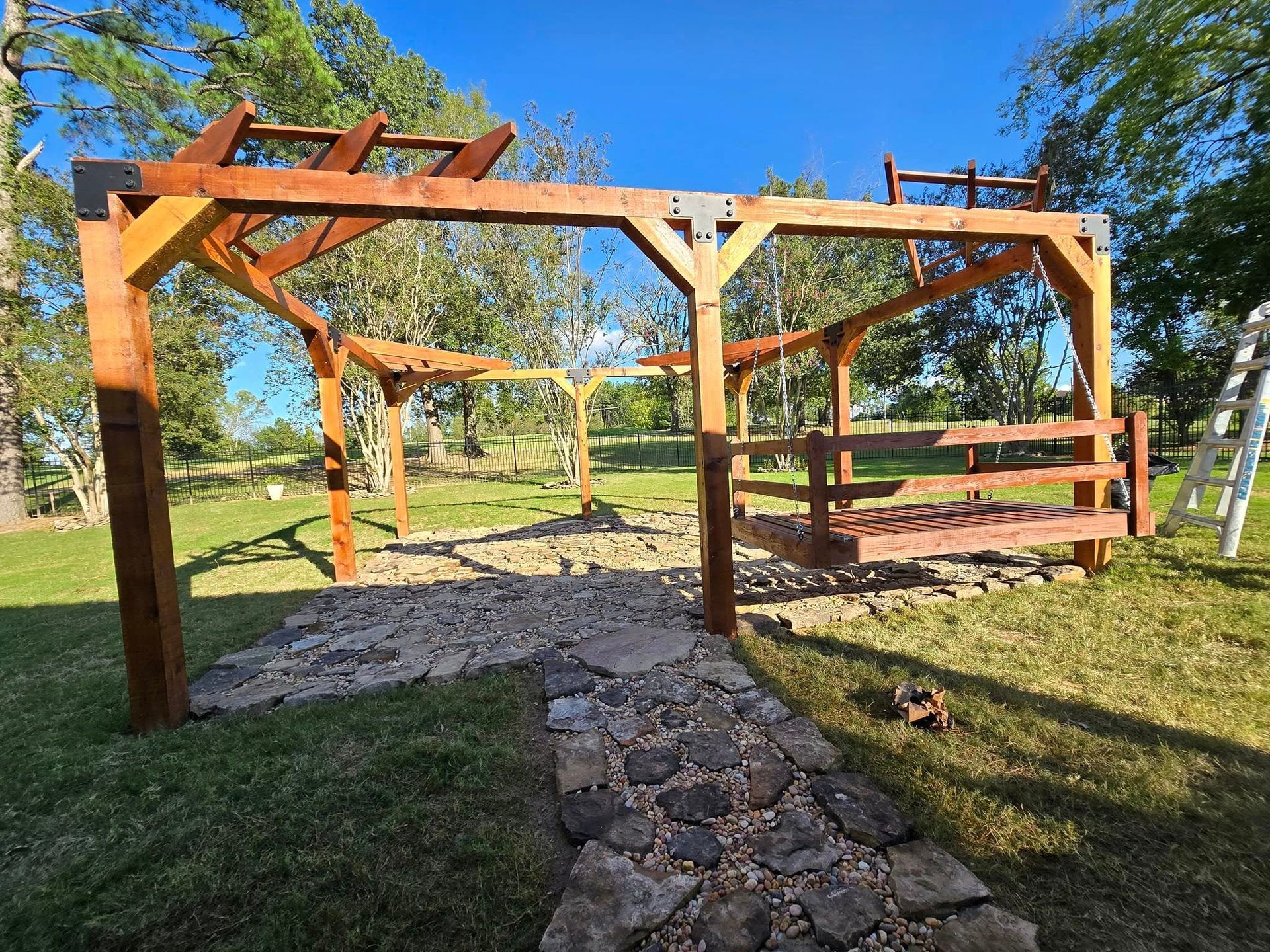 A wooden pergola is sitting in the middle of a lush green field.