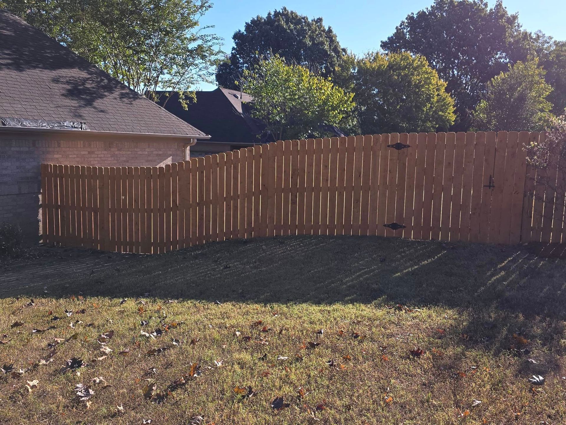 A wooden fence surrounds a grassy yard in front of a house
