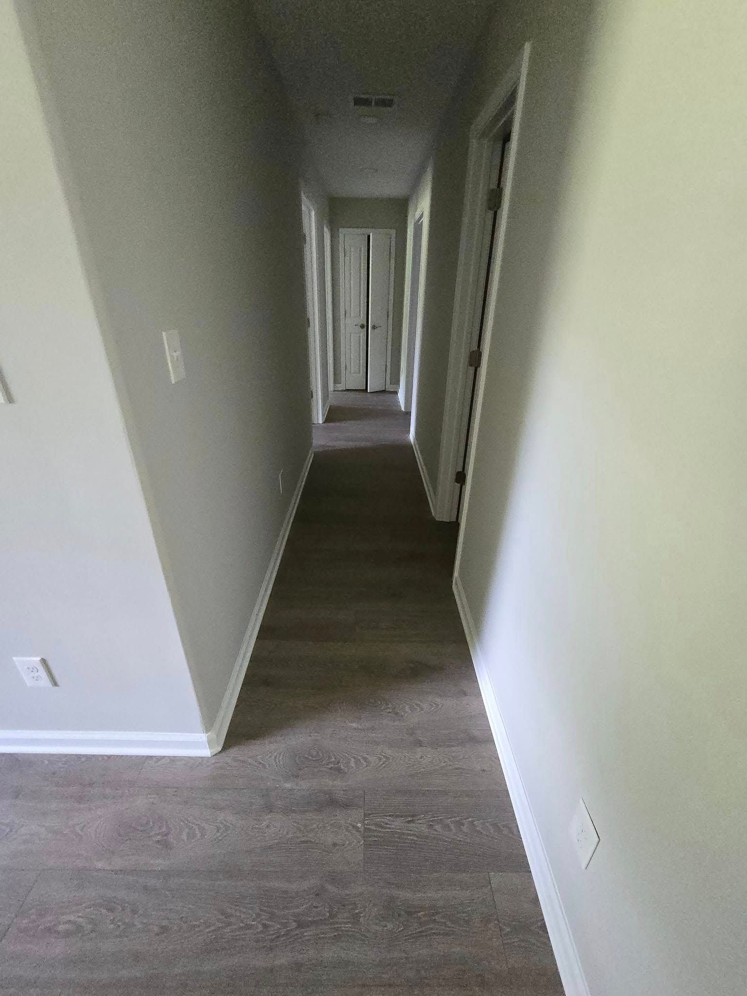 A long hallway in a house with hardwood floors and white walls.