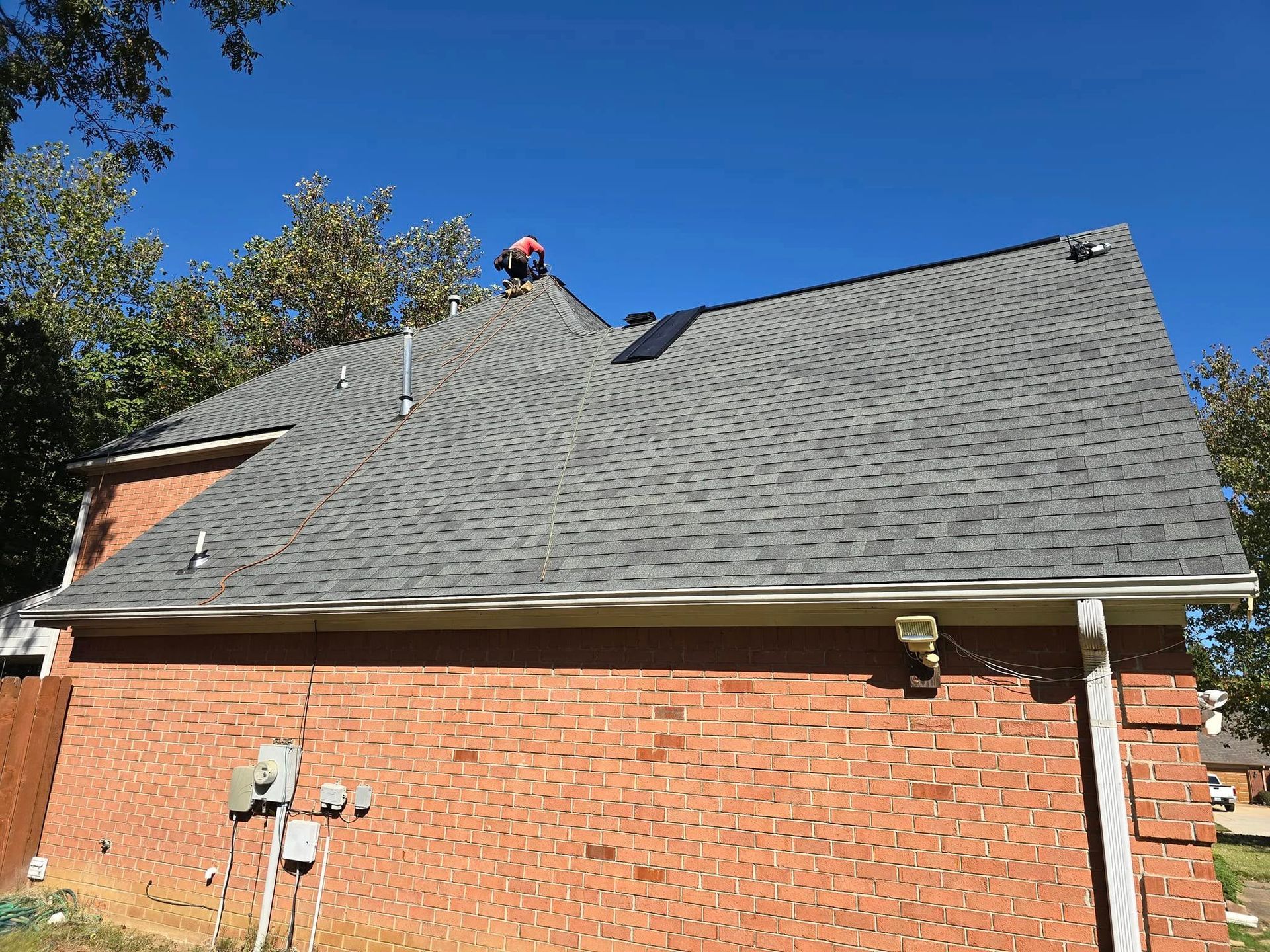 A man is working on the roof of a brick house.